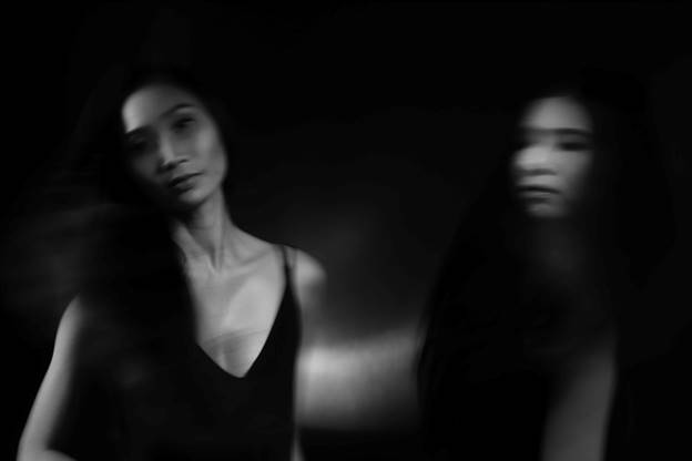 A grayscale artistic image depicts an Asian woman in focus beside a blurry copy. The woman is wearing a low-cut top, potentially discussing sensitive legal content.